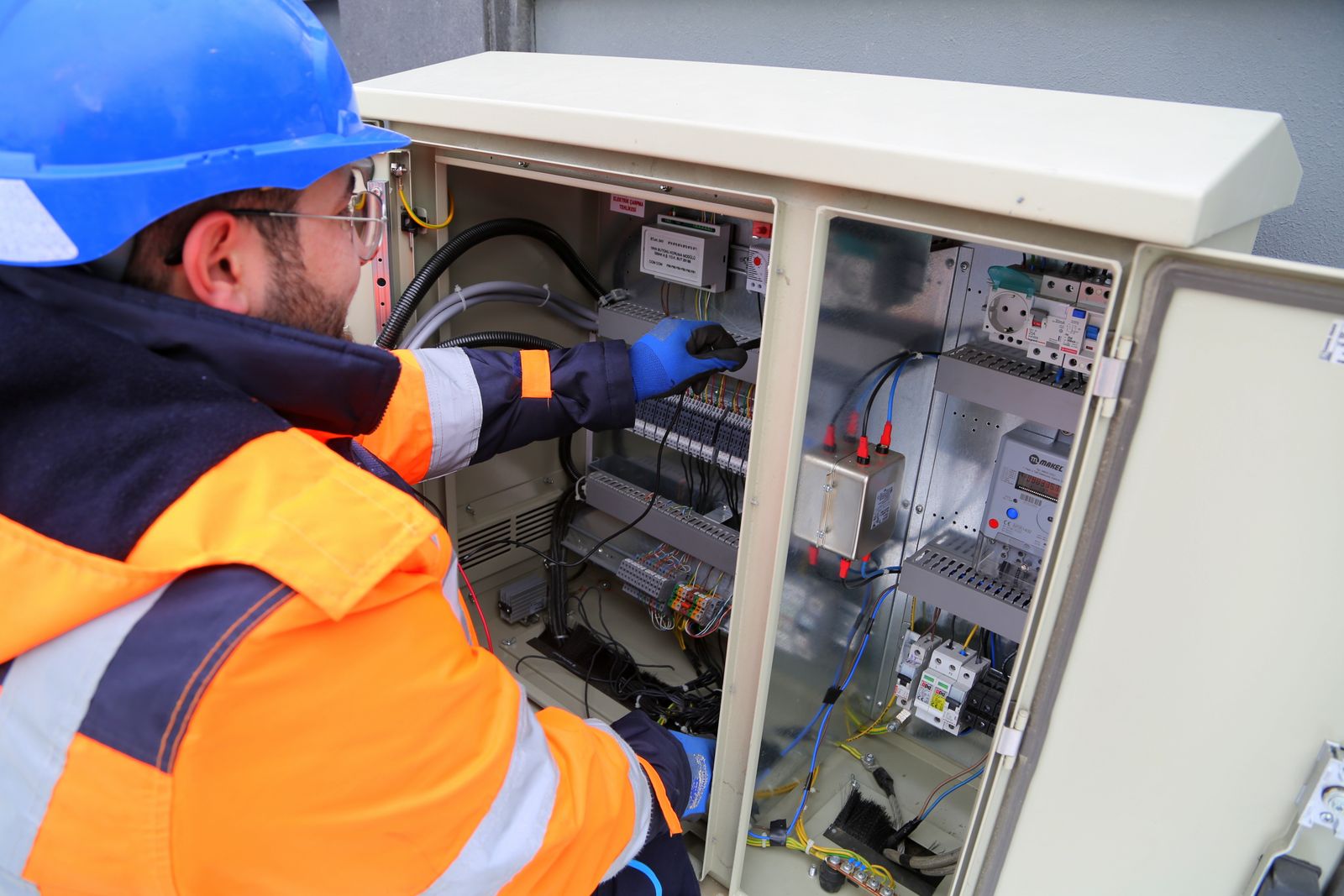 Stock photo of an electrician in a hard hat and safety vest working inside an outdoor electrical cabinet.