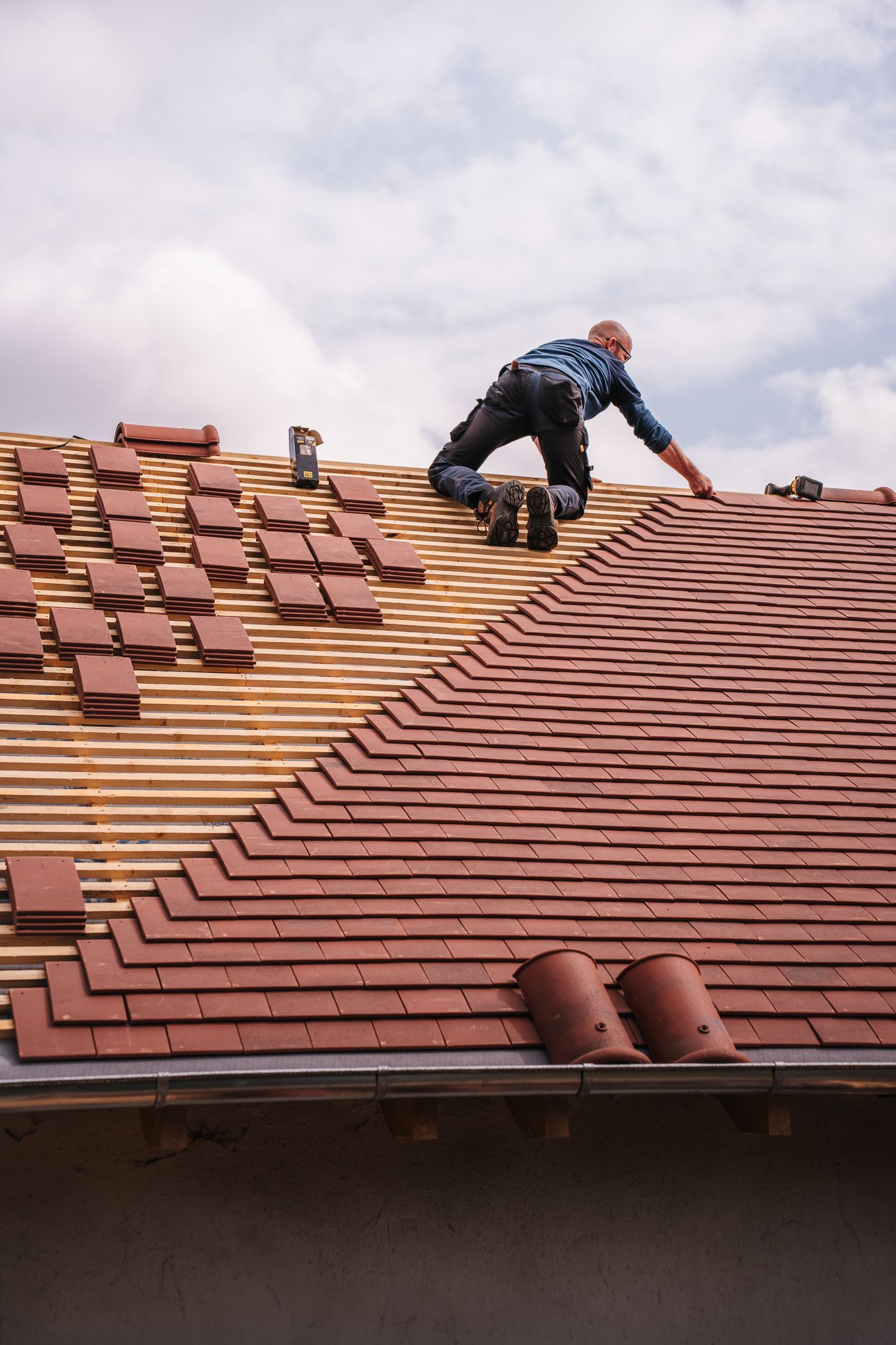 Stock photo of a roofer installing red roof tiles with the roof structure and materials visible.