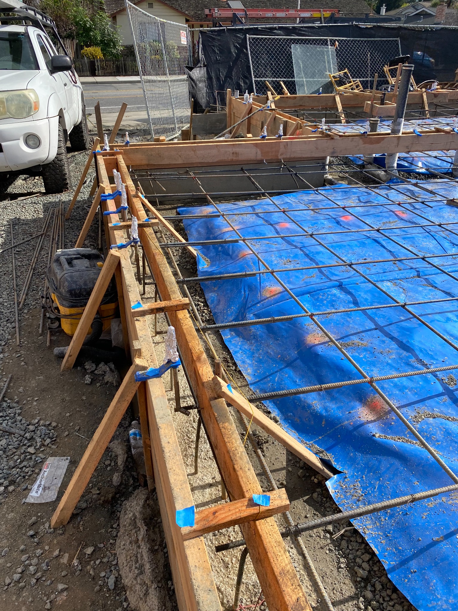 Steel reinforcing grid above blue sheet material within timber concrete forms, with pipe openings visible.