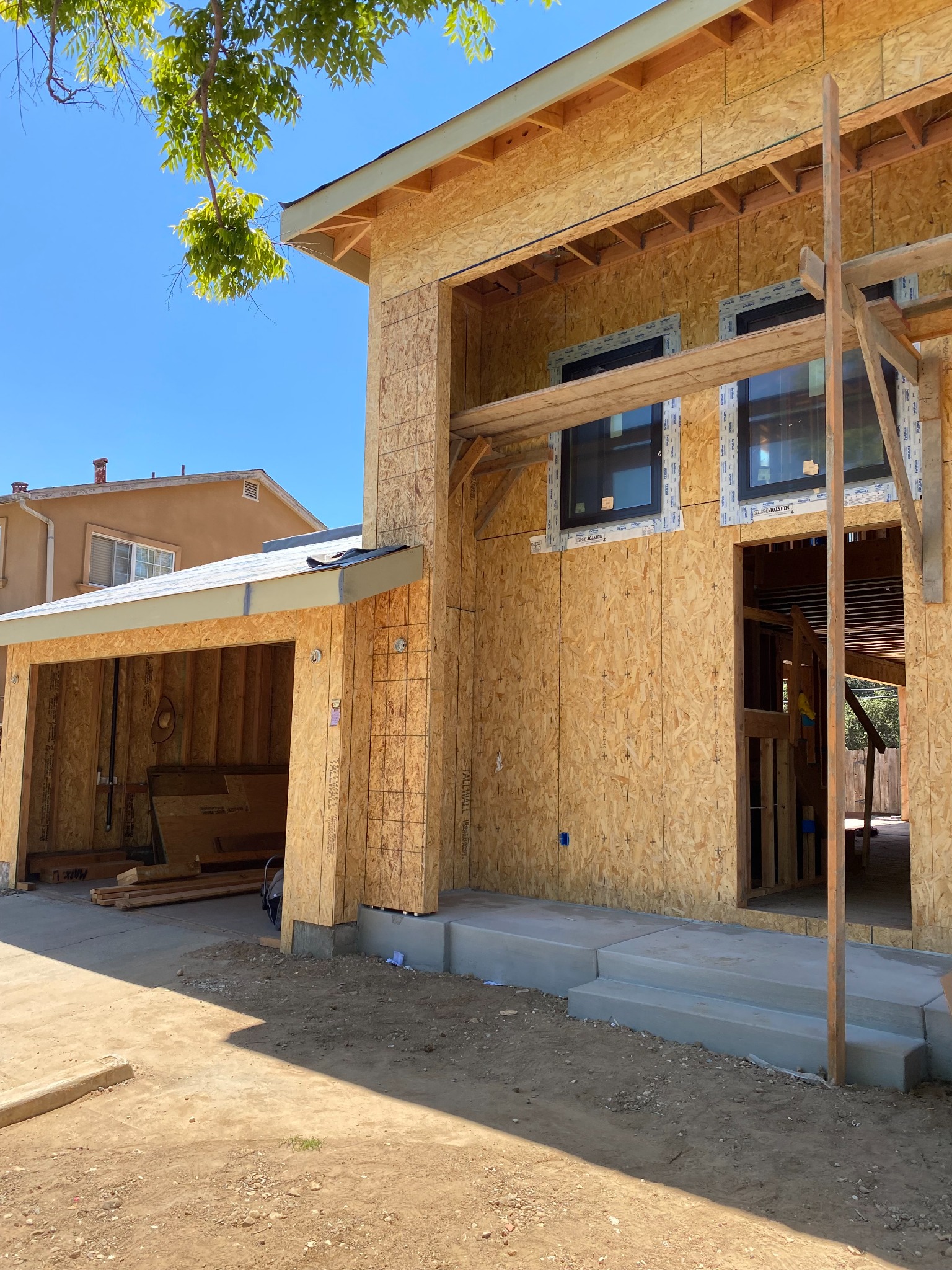 Building exterior under construction, with exposed wood sheathing, windows, an open garage and concrete entry steps.