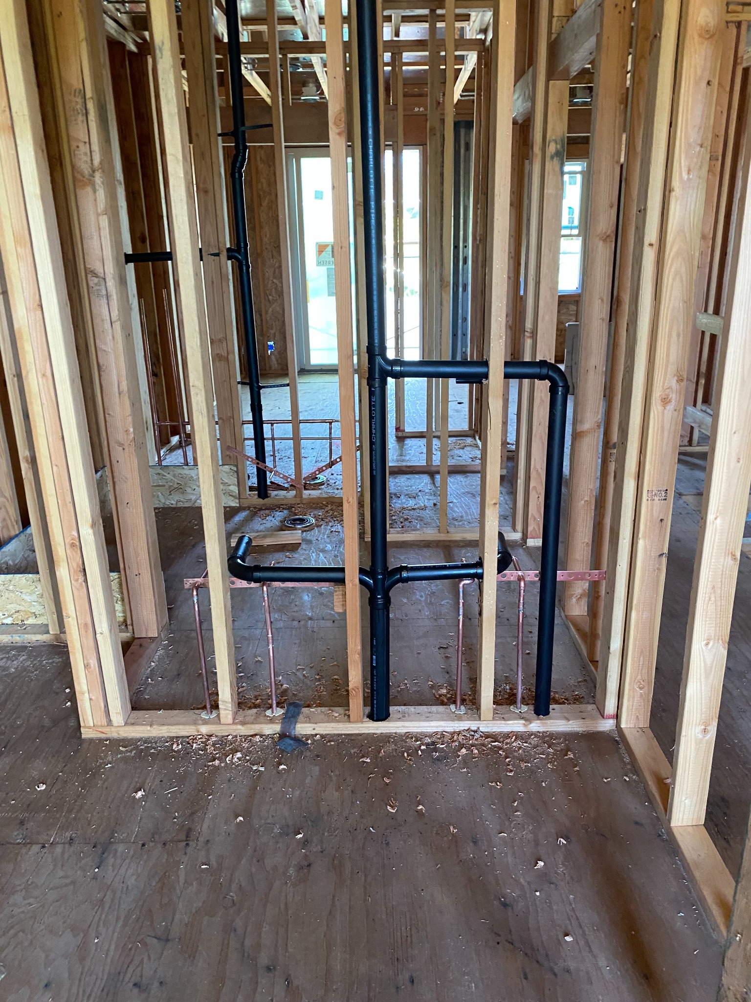 Interior timber wall framing with exposed black drain pipes and copper pipework.