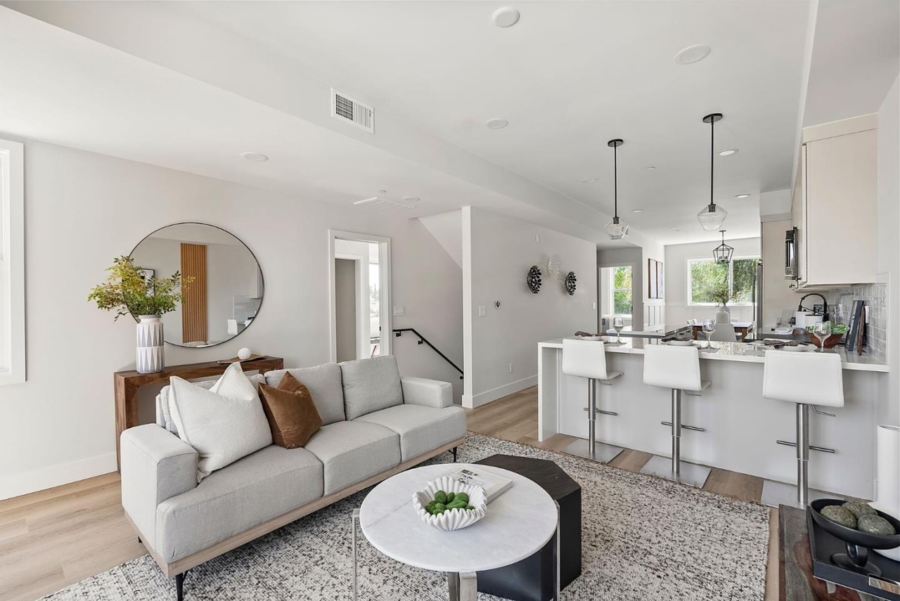Open living room beside a white kitchen with a breakfast bar and pendant lights.